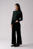 Woman wearing a green plaid shirt and black pants on a light gray background