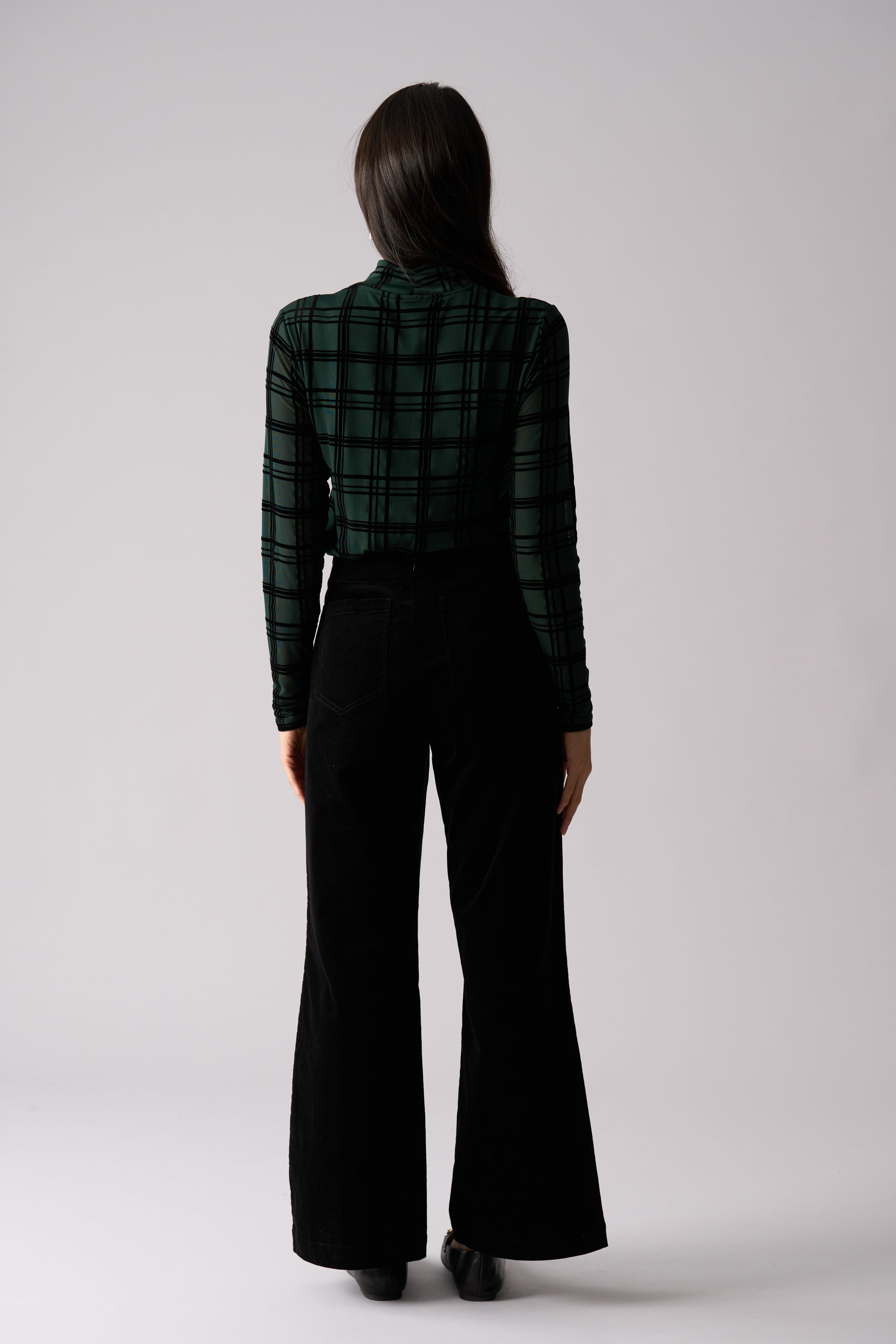 Person wearing a green plaid shirt and black flared pants on a white background