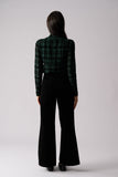 Person wearing a green plaid shirt and black flared pants on a white background