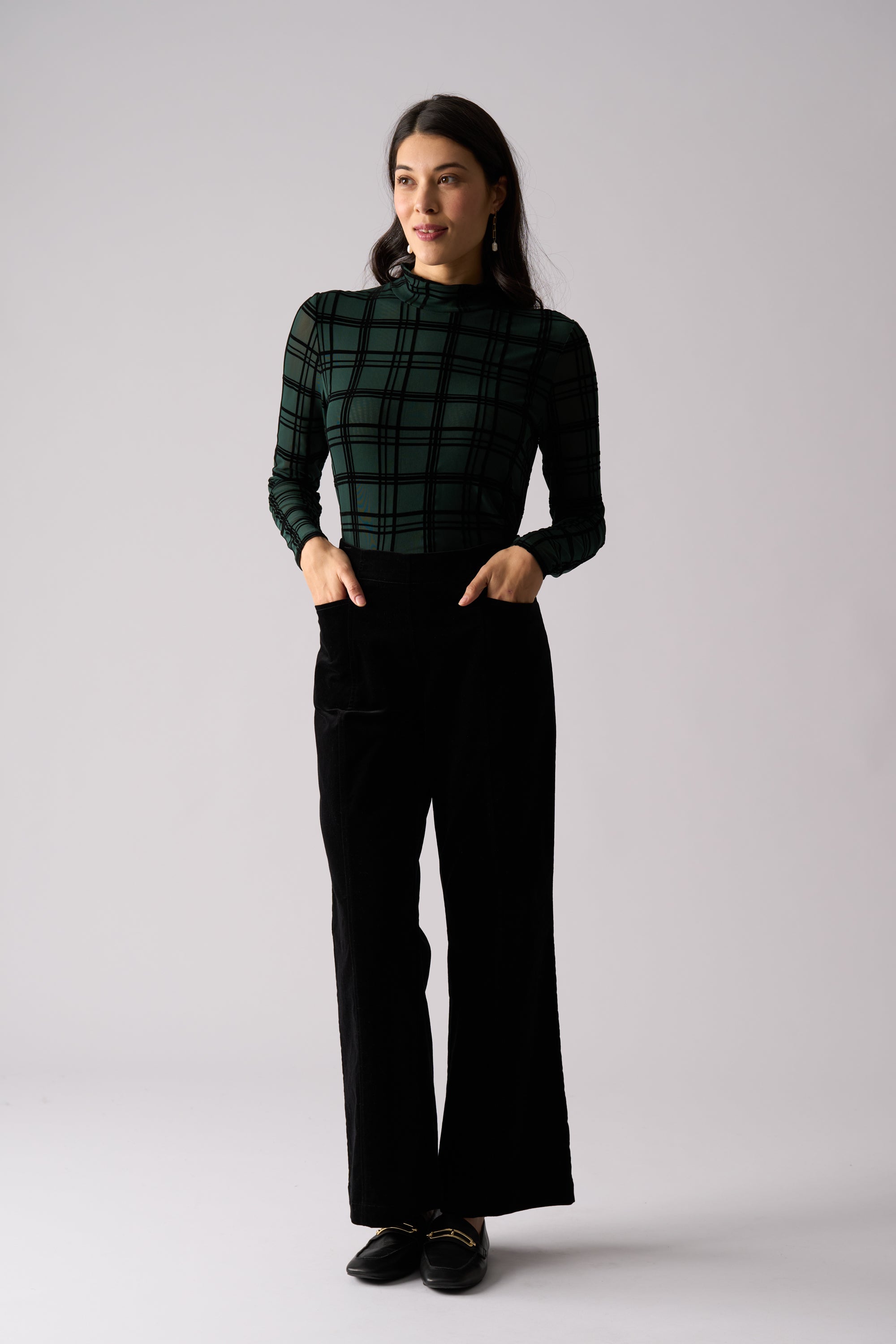 Woman wearing a green plaid top and black pants on a white background