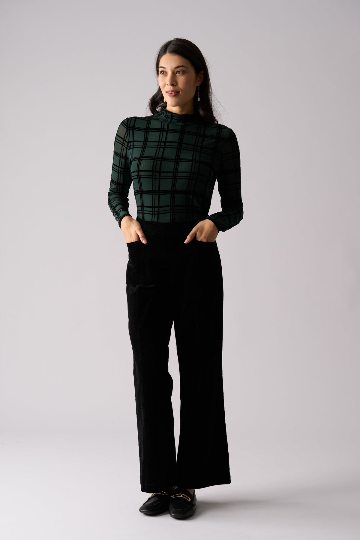 Woman wearing a green plaid top and black pants on a white background