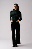 Woman wearing a green plaid top and black pants on a white background