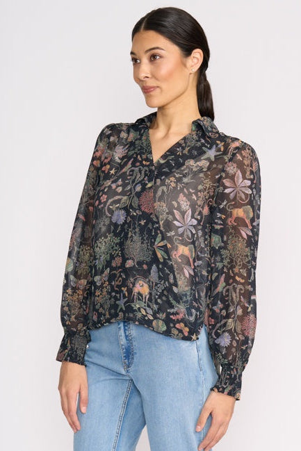 Woman wearing a floral blouse with long sleeves and light blue jeans on a white background