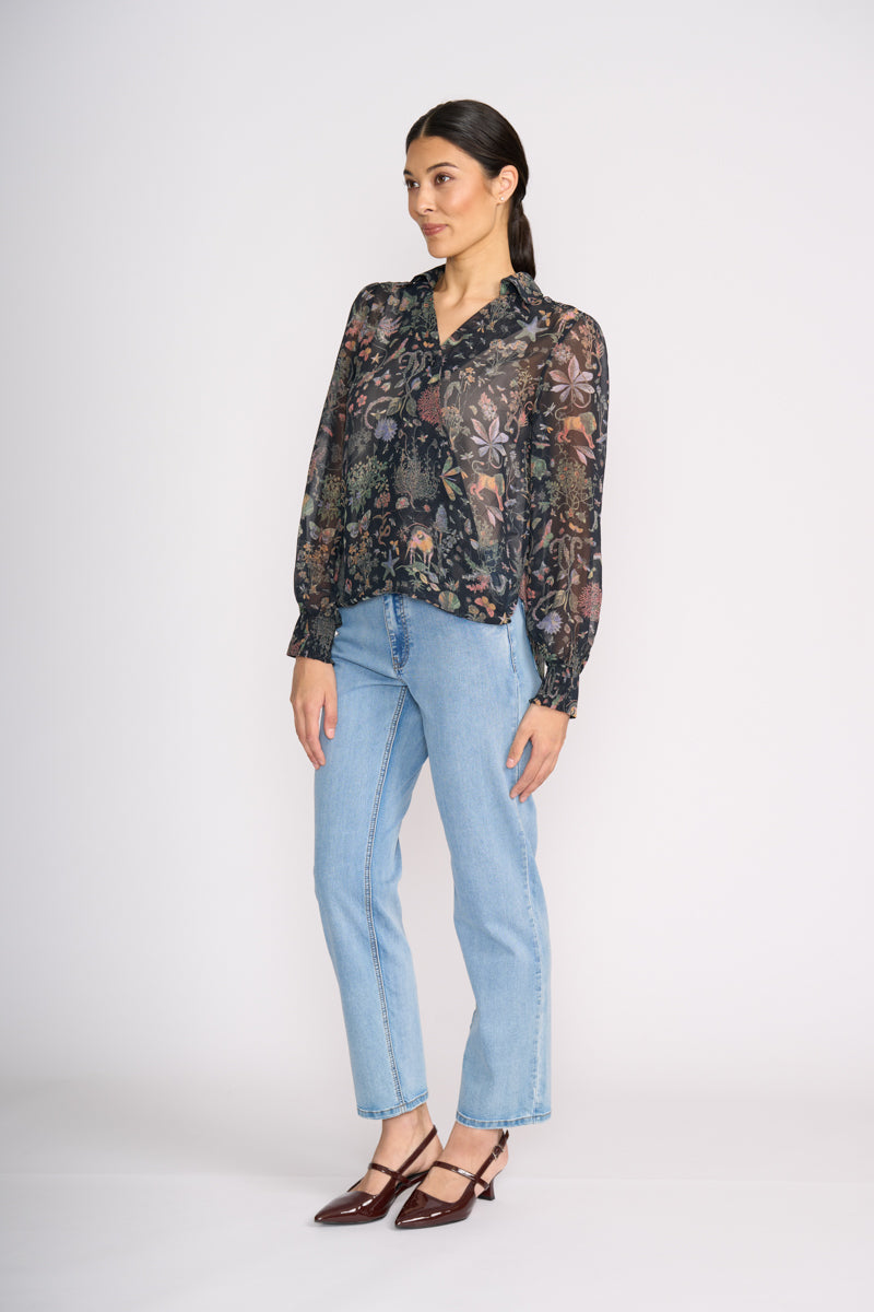 Woman wearing a floral sheer blouse and light blue jeans on a white background