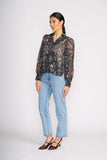 Woman wearing a floral sheer blouse and light blue jeans on a white background