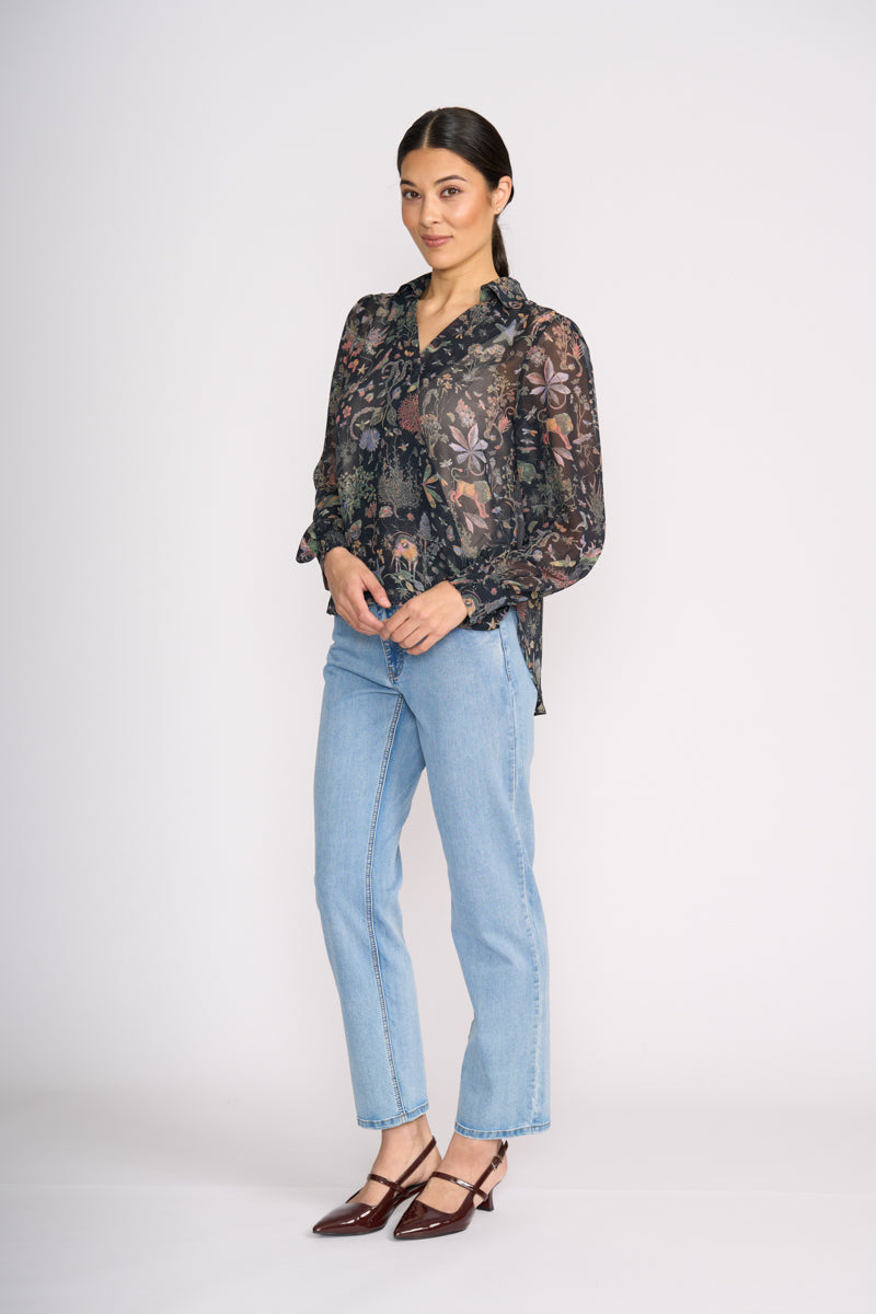 Woman wearing a sheer floral blouse and light blue jeans on a white background