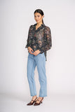 Woman wearing a sheer floral blouse and light blue jeans on a white background