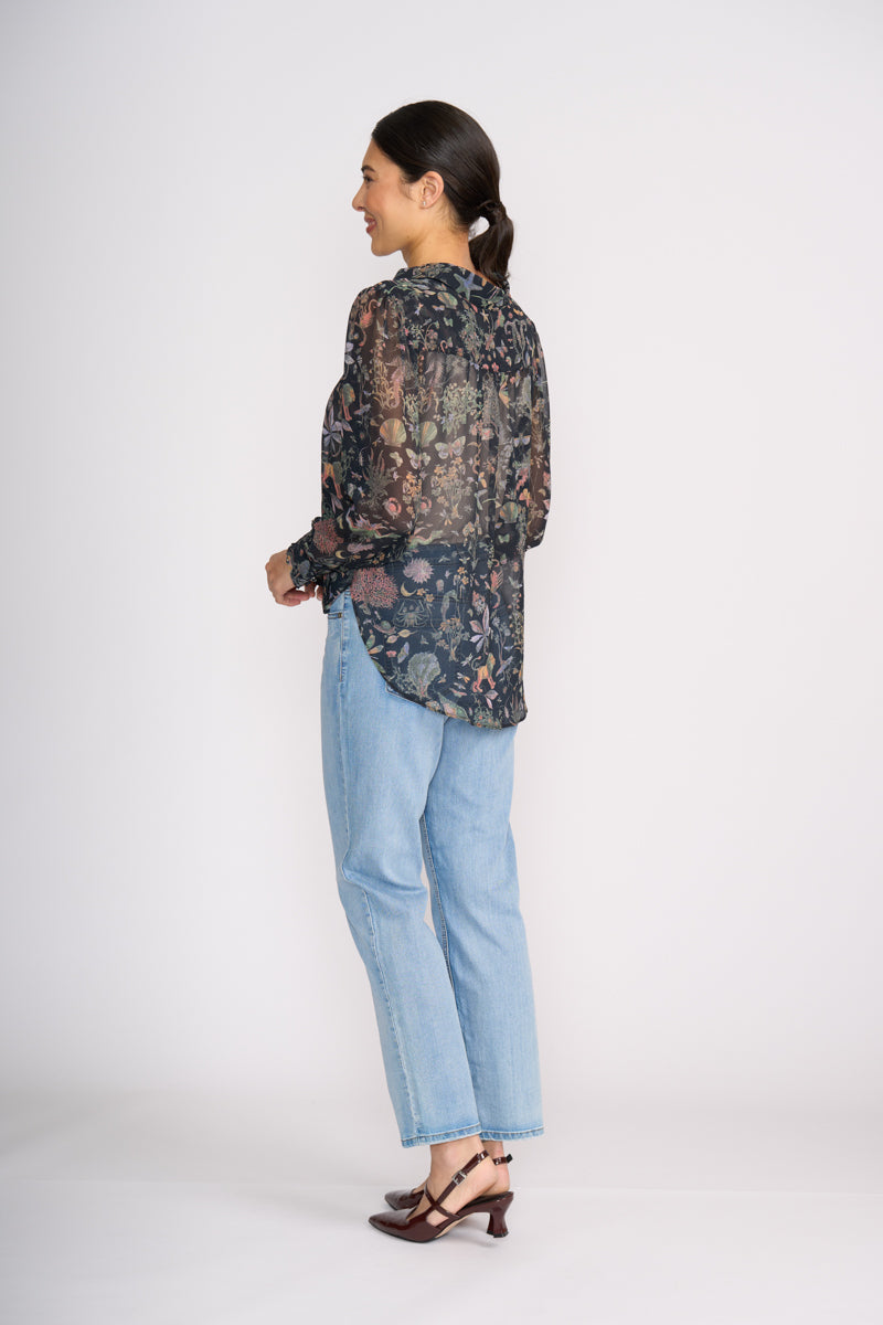 Woman wearing a patterned blouse and light blue jeans on a white background