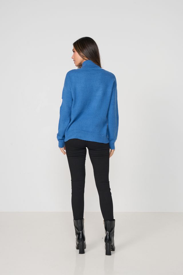A woman is shown from the back wearing a bright blue mock-neck knit sweater, black skinny pants, and black leather ankle boots, standing against a plain white studio background.