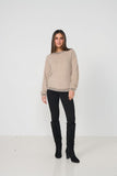 Woman wearing a beige sweater and black pants with knee-high boots on a white background