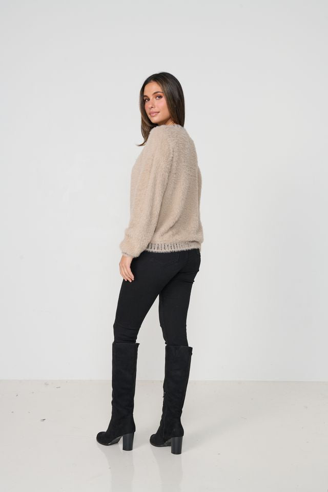 Woman wearing a beige sweater and black pants with knee-high boots on a white background