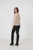 Woman wearing a beige sweater and black pants with knee-high boots on a white background