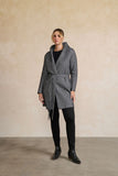 Person wearing a gray coat standing against a beige wall.