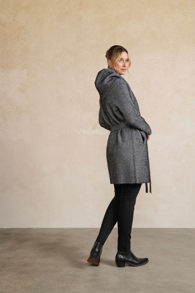 Woman wearing a gray patterned coat against a beige wall