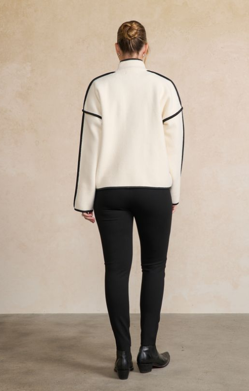 Person wearing a white jacket with black accents and black pants on a beige background