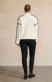 Person wearing a white jacket with black accents and black pants on a beige background