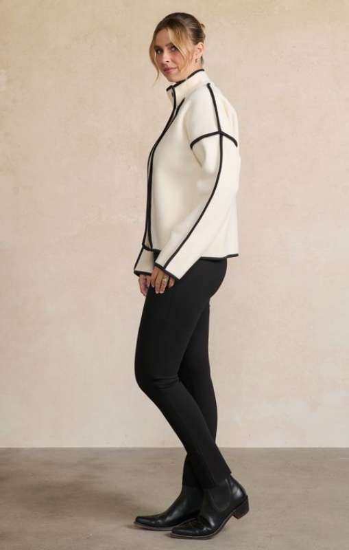 Person wearing a white jacket with black accents and black pants against a beige background