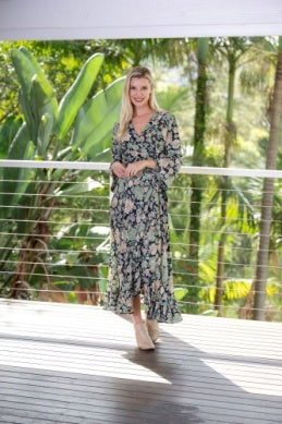 Woman in a floral dress standing on a wooden deck with greenery in the background