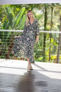 Woman in a floral dress standing on a wooden deck with greenery in the background