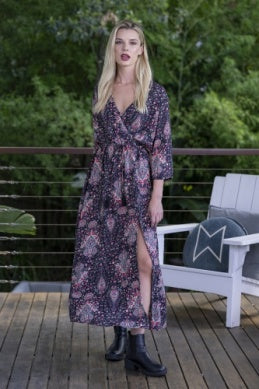 Woman in a floral dress standing on a wooden deck with greenery in the background