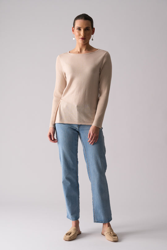 Woman wearing a beige sweater and blue jeans on a plain background