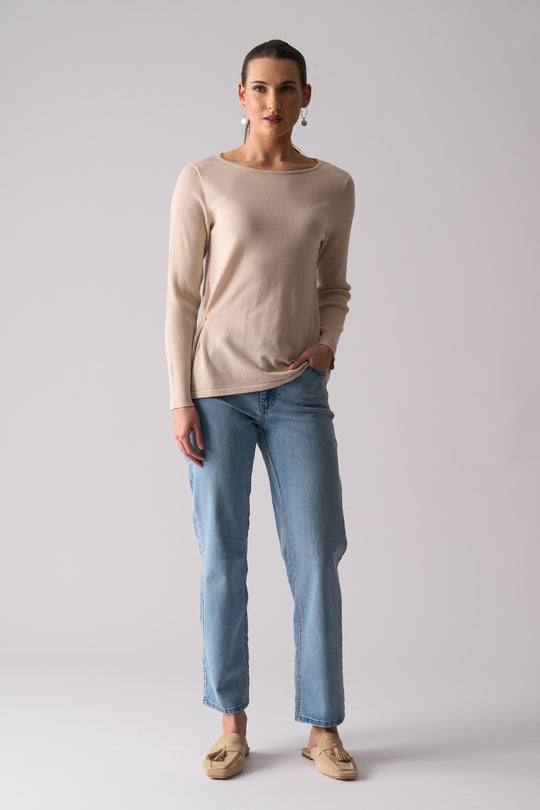 Woman wearing a beige sweater and blue jeans on a plain background