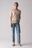 Woman wearing a beige sweater and blue jeans on a plain background