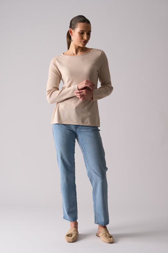 Woman wearing a beige sweater and light blue jeans on a plain background