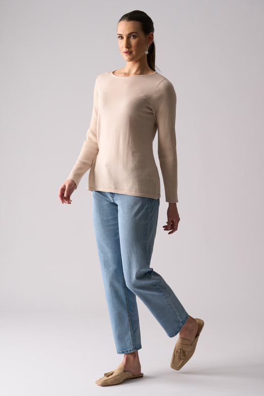 Woman wearing a beige sweater and light blue pants on a plain background