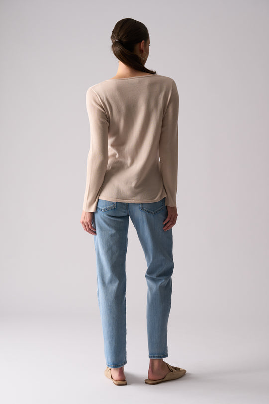 Person wearing a beige long-sleeve shirt and light blue jeans on a plain background