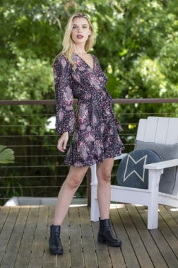 Woman in a floral dress standing on a wooden deck with greenery in the background
