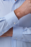 Close-up of a man wearing a light blue and white striped dress shirt, showing the fabric texture and buttoned cuffs.