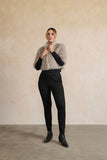 Person wearing a gray knitted sweater and black pants against a beige background