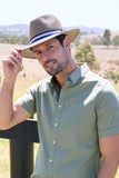 Man wearing a green shirt and straw hat with a blue band, standing outdoors.