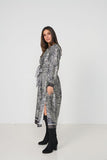 A woman modeling a long-sleeved wrap-style midi dress with a black and white zebra print, paired with black knee-high boots, against a plain white studio background.