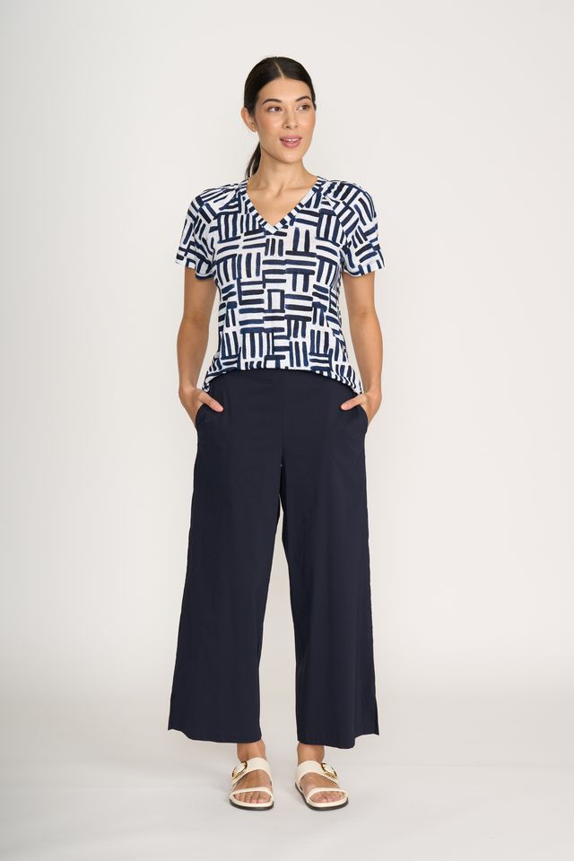 Woman wearing a black and white patterned top and navy pants on a white background