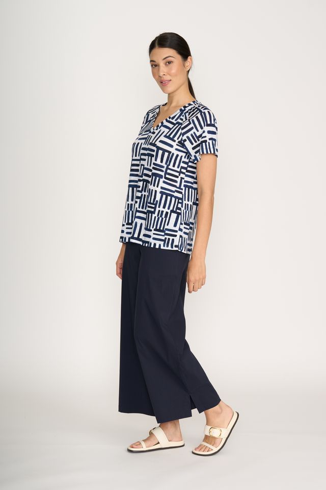 Woman wearing a patterned shirt and dark pants on a white background