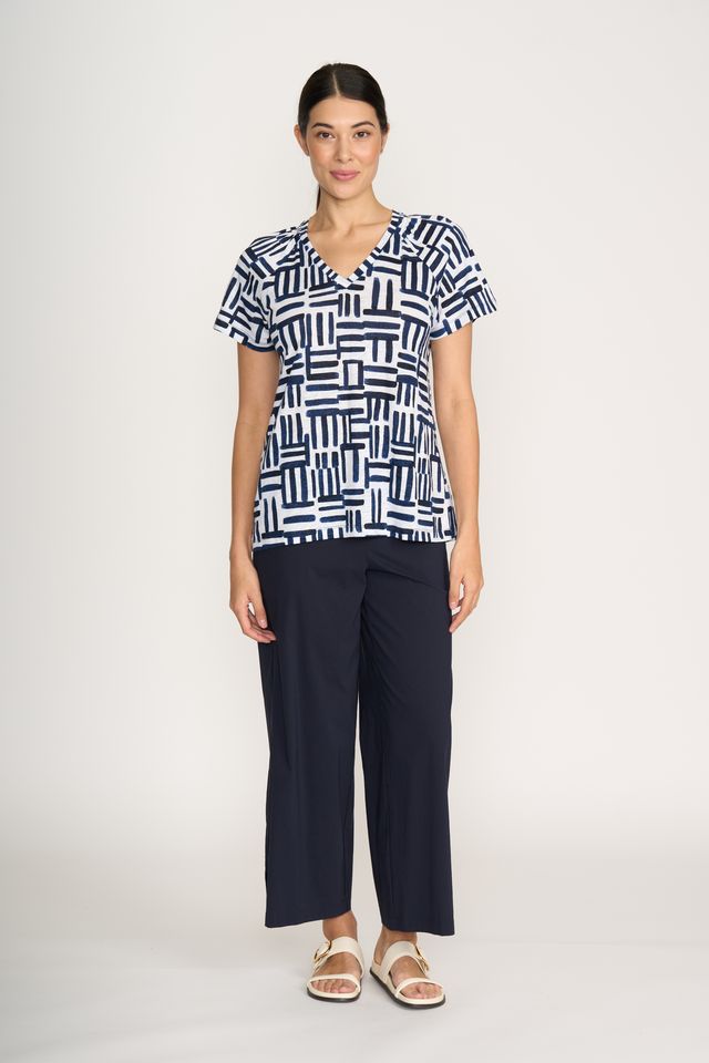 Woman wearing a black and white patterned top and navy pants on a white background