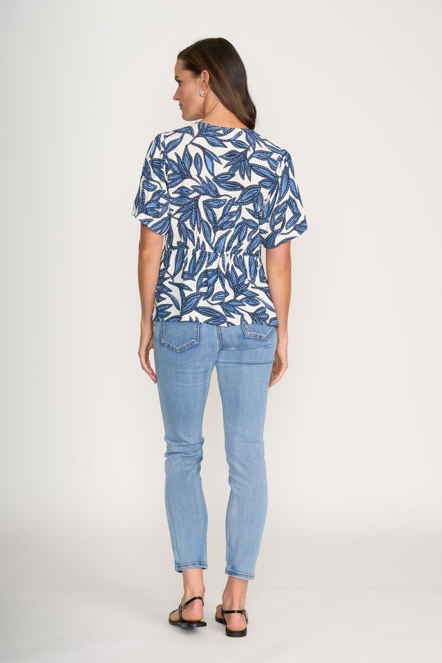 Woman wearing a blue leaf-patterned shirt and light blue jeans on a white background