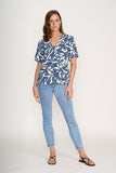 Woman wearing a blue and white patterned top and light blue jeans on a white background