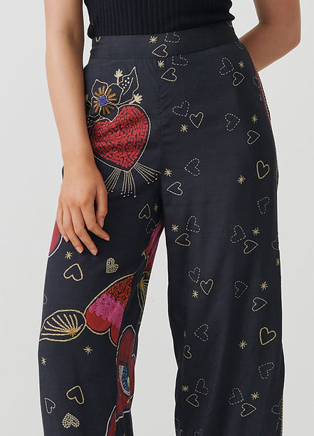 A close-up of a person wearing dark navy wide-leg pants with a colorful heart and floral print, paired with a black ribbed top against a light gray studio background.