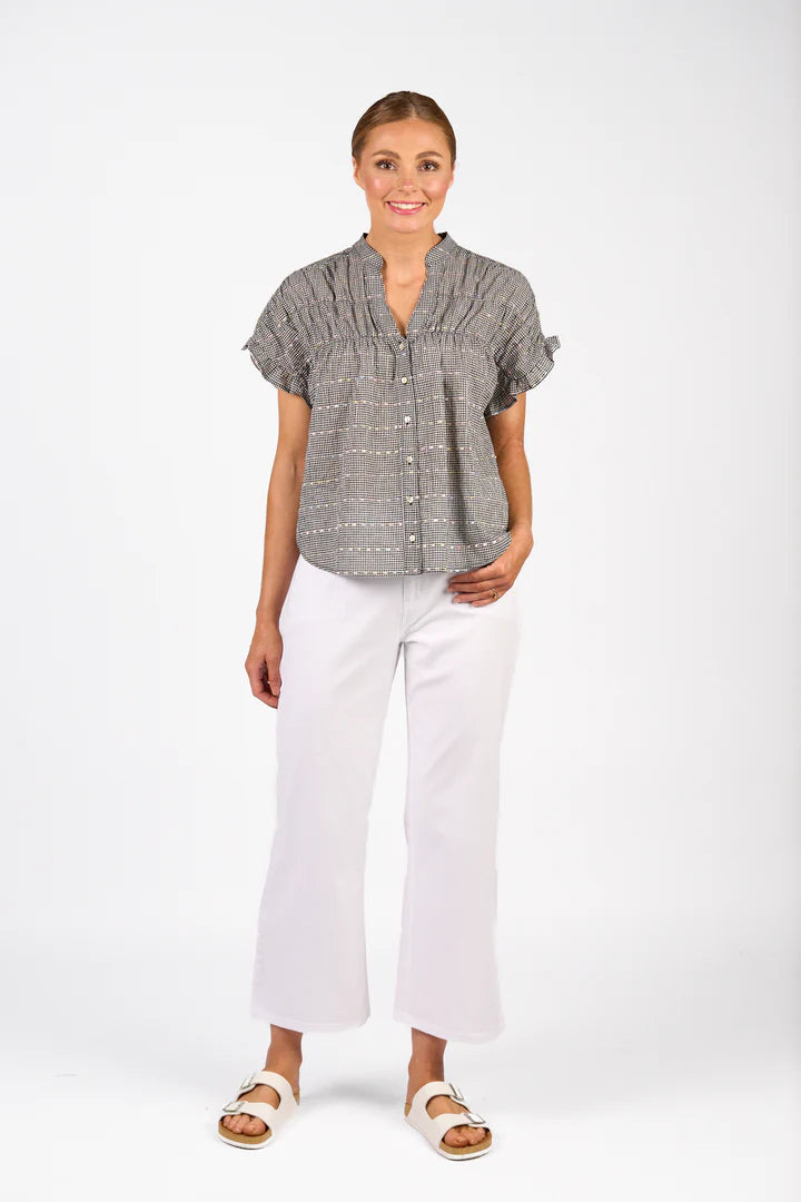 Woman wearing a gray patterned blouse and white pants on a white background