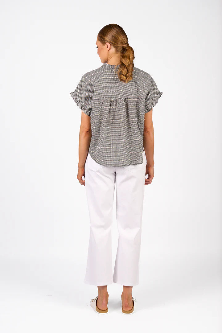 Woman wearing a gray patterned blouse and white pants on a white background