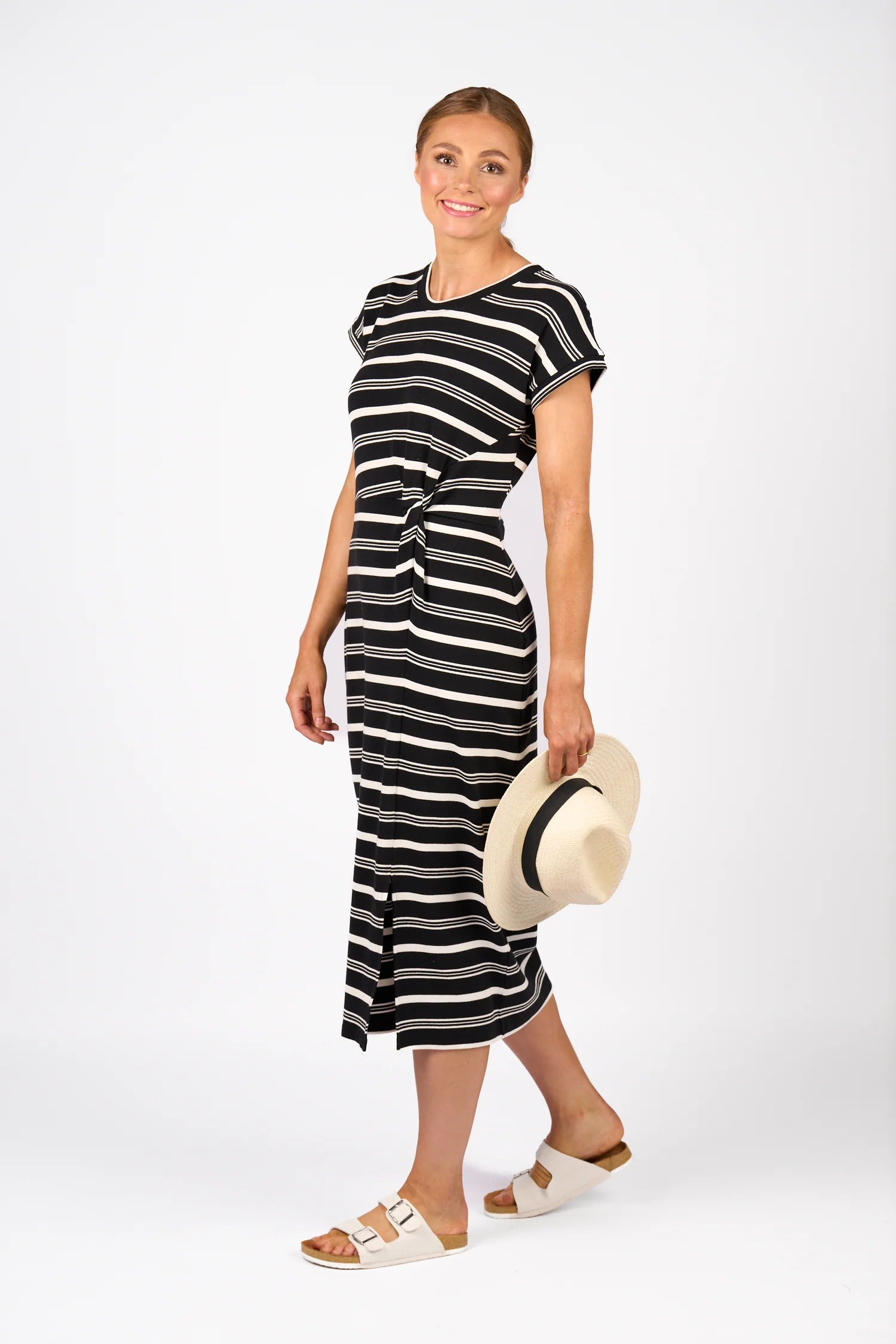 Woman wearing a black and white striped dress holding a hat on a white background