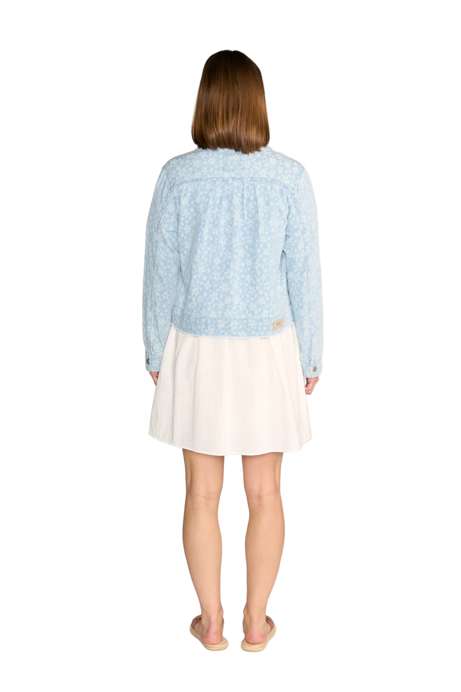 Person wearing a light blue patterned shirt and white skirt on a plain background