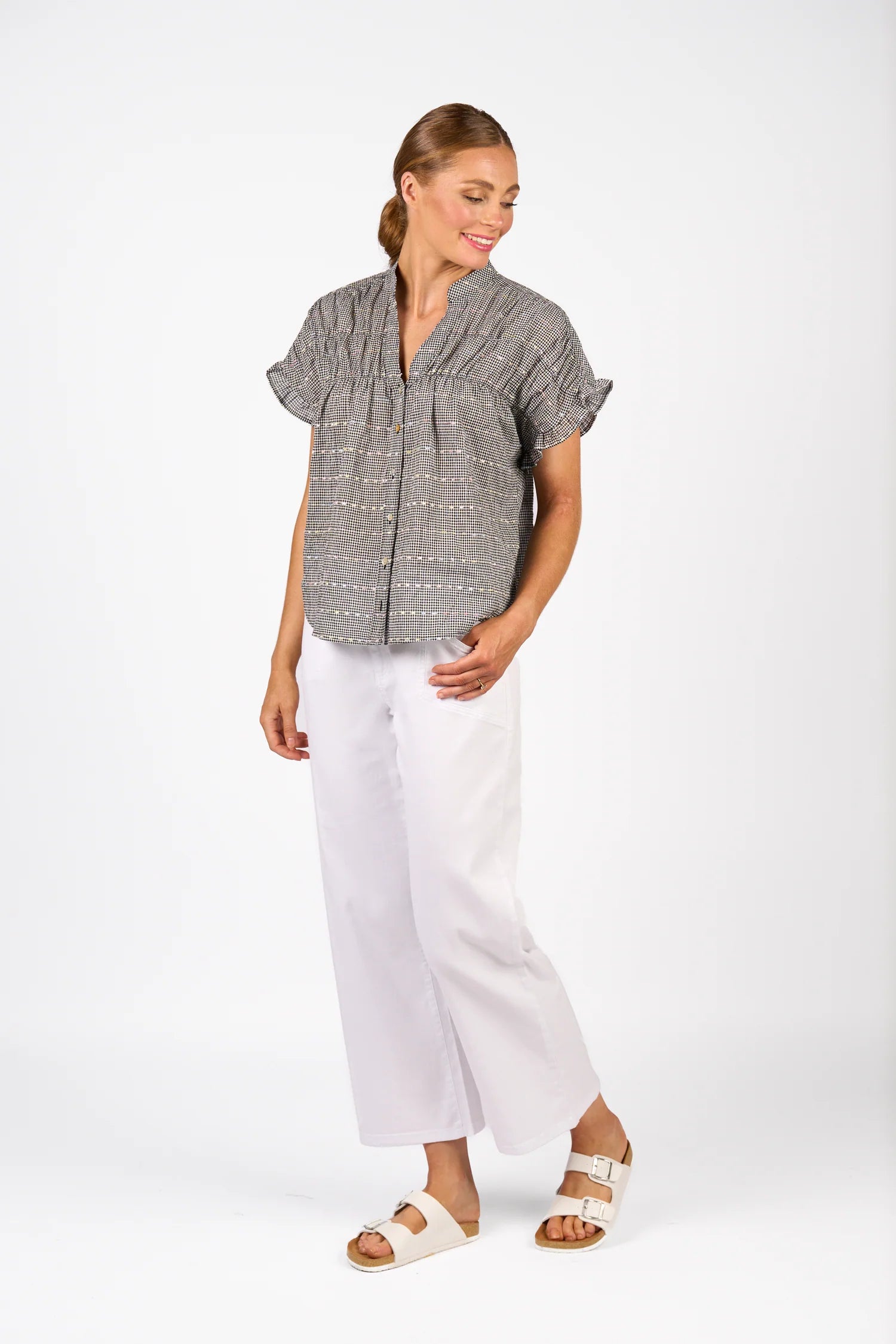Woman wearing a gray patterned shirt and white pants on a white background