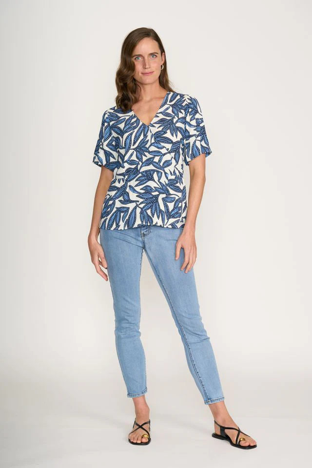 Woman wearing a blue and white patterned blouse and light blue jeans on a white background