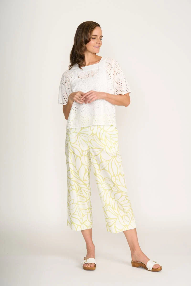 Woman wearing a white lace top and yellow patterned pants on a white background
