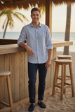 Man standing by a wooden bar on a beach with palm trees and ocean in the background