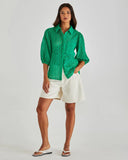 Woman wearing a green patterned shirt and white shorts on a plain background